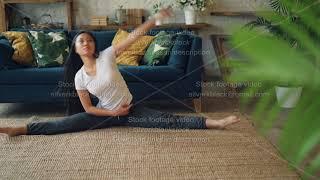 Flexible Asian girl is doing yoga at home sitting on floor and stretching legs and body exercising