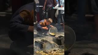 Palestinian child gathers pasta off the ground at community kitchen